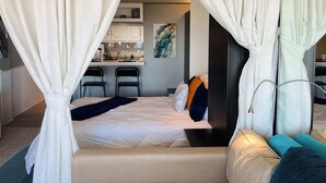 Un dormitorio con cama, mesita de noche, espejo y vista a una zona de cocina.