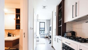 Una cocina moderna con estufa, horno y armarios. Se observa un área de comedor con sofá y mesa al fondo.
