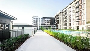 Un moderno edificio residencial con piscina, un paseo techado y una fila de plantas.