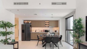 A modern kitchen with a dining area, featuring a built-in oven, a refrigerator, and a dining table with chairs.