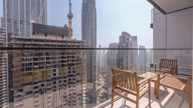 A balcony with a view of a cityscape, including high-rise buildings and construction cranes.