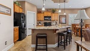 Une cuisine moderne avec des meubles en bois, un réfrigérateur noir, un plan de travail en granit et des luminaires suspendus.