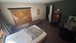 Une chambre à coucher avec un lit, une carte accrochée au mur, un banc, une commode et une porte donnant sur une autre pièce.
