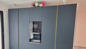 A modern kitchen with a built-in oven and microwave, grey cabinets, and a window with a view. - Le 46 Cosy, modern villa.  Between Paris, Disneyland and Parc Asterix (Villiers-sur-Marne)