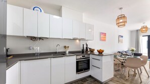 A modern kitchen with white cabinets, a built-in oven, and a dining area with a table and chairs. - Casa Variza, tu refugio en Playa Blanca (Playa Blanca)