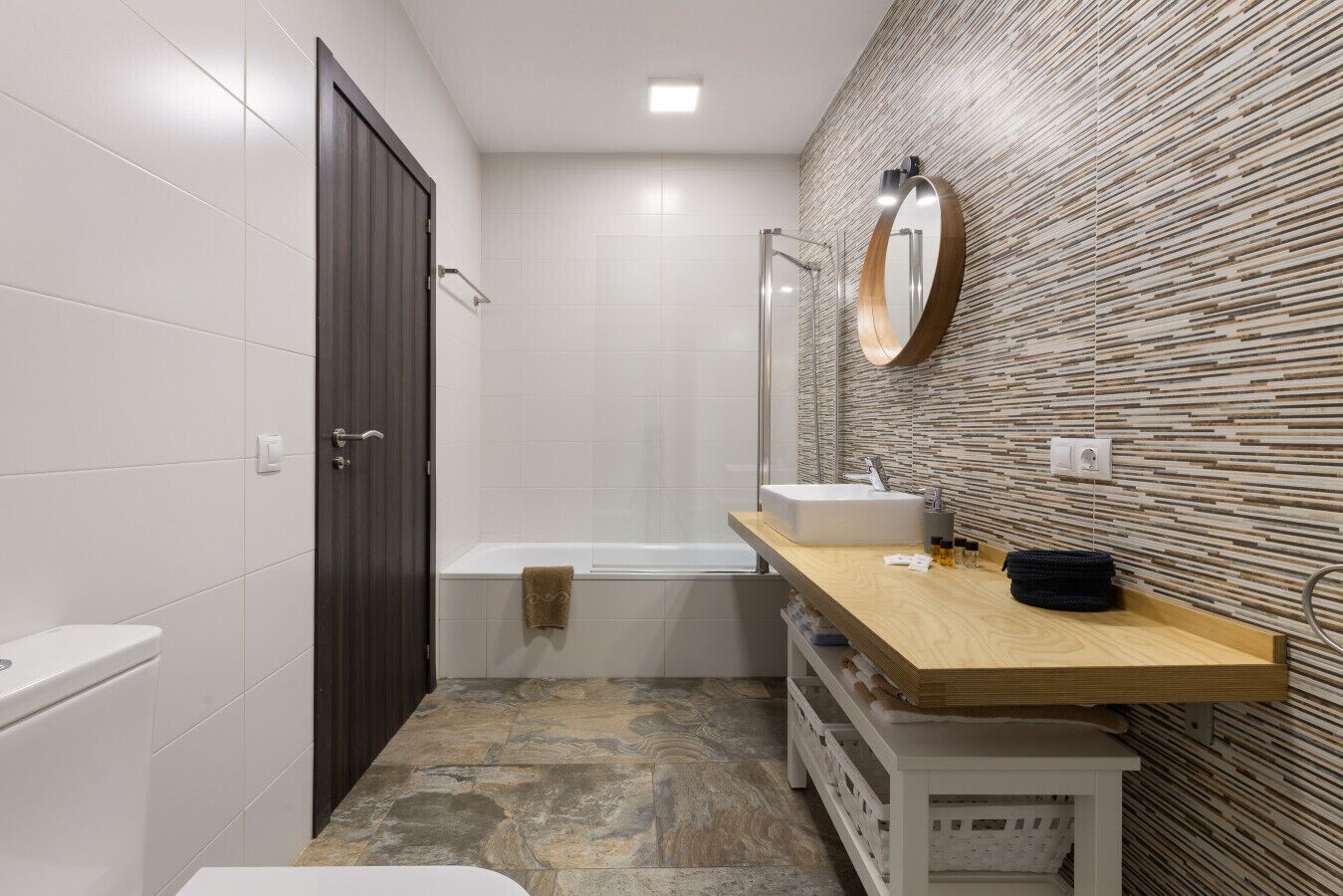 Un baño moderno con tocador de madera, lavamanos blanco y bañera.