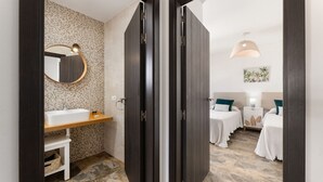 A bathroom with a sink, mirror, and tiled walls. There are two beds with white bedding and a nightstand with a lamp. - Casa Variza, tu refugio en Playa Blanca (Playa Blanca)