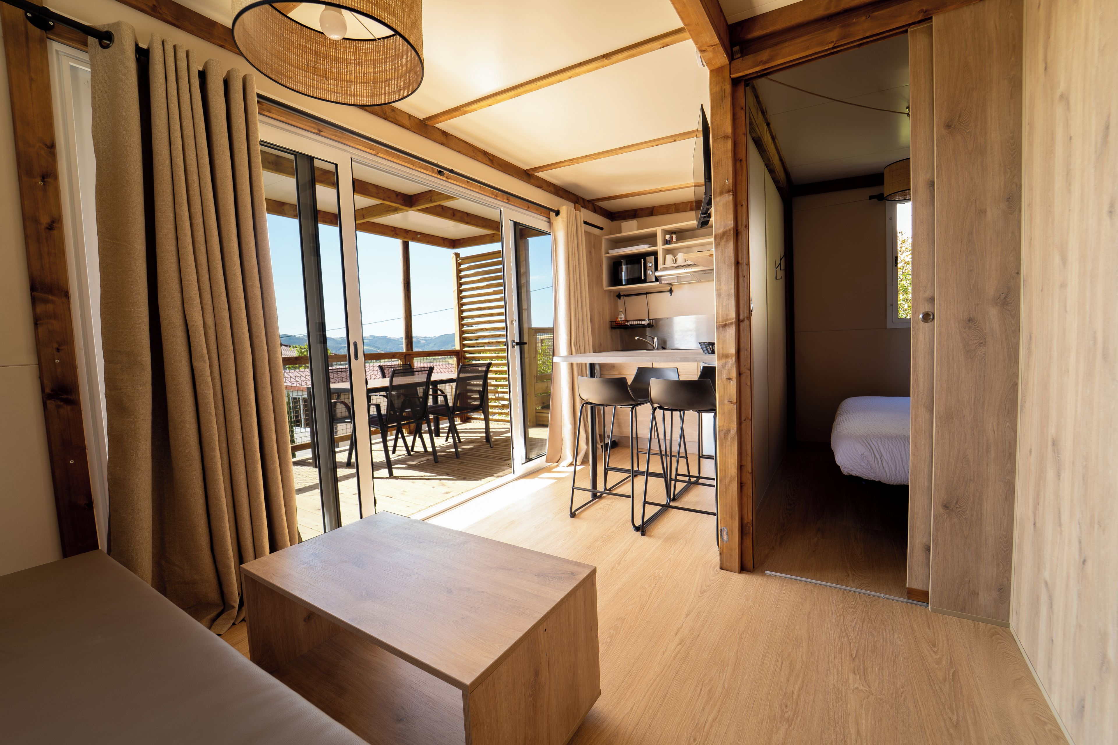 A cozy room with a wooden floor, a small table, a sofa, and a sliding glass door leading to an outdoor area with a table and chairs.