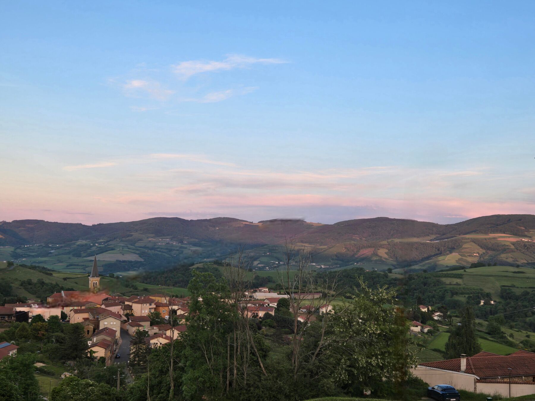 Un village avec un clocher d’église, entouré de collines douces et de verdure.