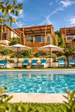 A pool area with lounge chairs and umbrellas, surrounded by a wooden deck and greenery. - Tiny d'Monts (Brullioles)