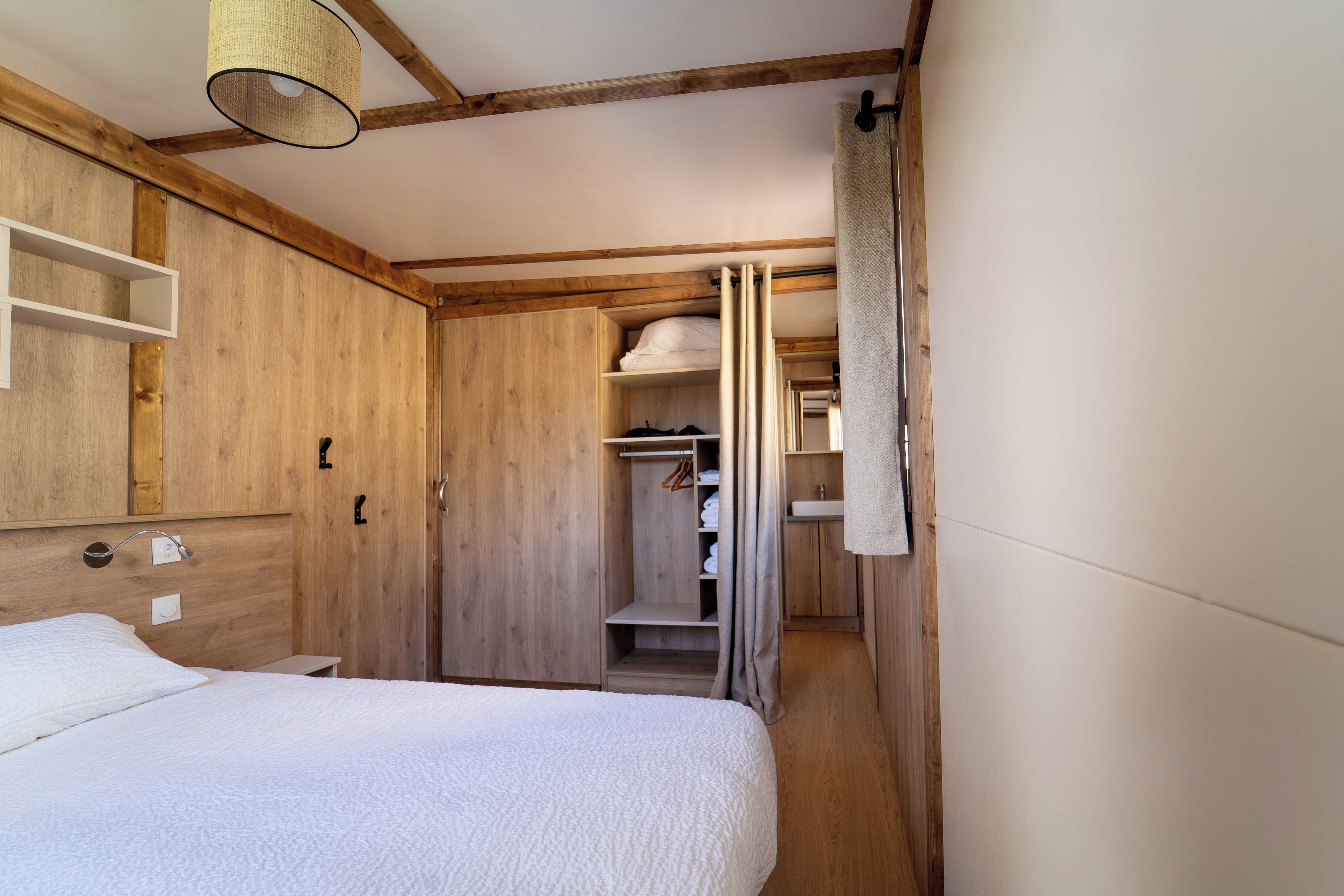 A bedroom with a wooden headboard, a bed with white bedding, a hanging light fixture, and a closet with hanging space.