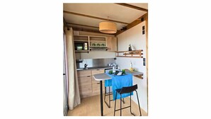 A compact kitchen with a microwave, sink, and wooden cabinets. There is a small dining area with a table and two chairs. - Tiny d'Monts (Brullioles)