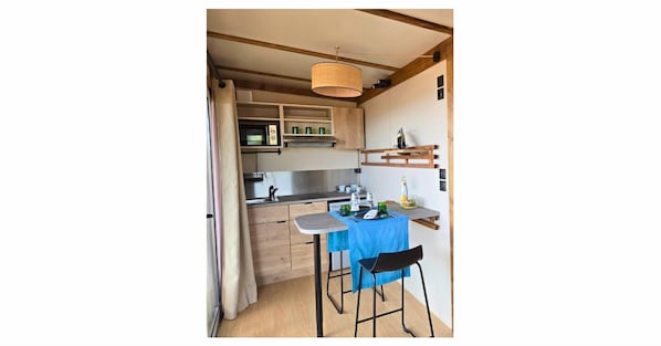 Een praktische keuken met een magnetron, spoelbak en houten kastjes. Er is een klein eethoekje met een tafel en twee stoelen.