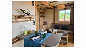A cozy room with a dining table set for two, a sofa with cushions, a laptop on a side table, and a bottle of wine on a shelf. - Tiny d'Monts (Brullioles)