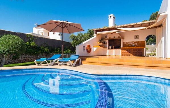 Une piscine aux carreaux bleus, des chaises longues et un espace patio doté d’un toit carrelé.