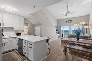 A modern kitchen with white cabinets, a built-in dishwasher, and a dining area with a wooden table and benches.