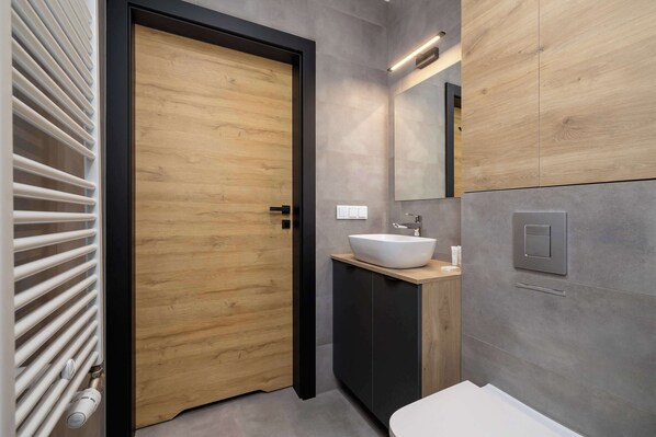 A modern bathroom with a wooden door, a white sink, and a large mirror.