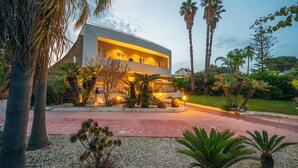 A modern building with a flat roof and multiple balconies, surrounded by palm trees and well-maintained landscaping. - Pink Moon Villa. Private Pool. Close to the Beach. 10 guests. Luxury. (Fontane Bianche)