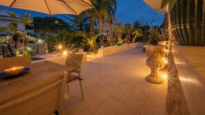 An outdoor patio area with a table and chairs, surrounded by potted plants and a large urn. - Pink Moon Villa. Private Pool. Close to the Beach. 10 guests. Luxury. (Fontane Bianche)