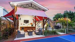 Un espace extérieur aménagé avec un patio, un barbecue, des sièges et un court de tennis.