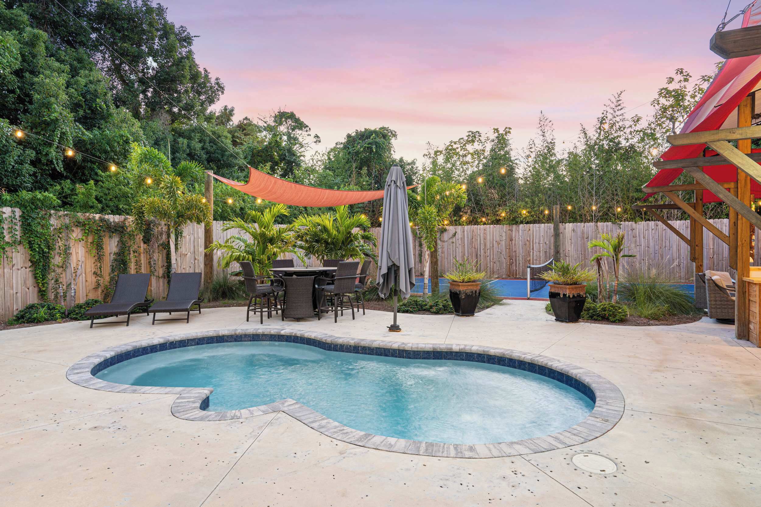 A backyard with a swimming pool, outdoor furniture, and string lights.
