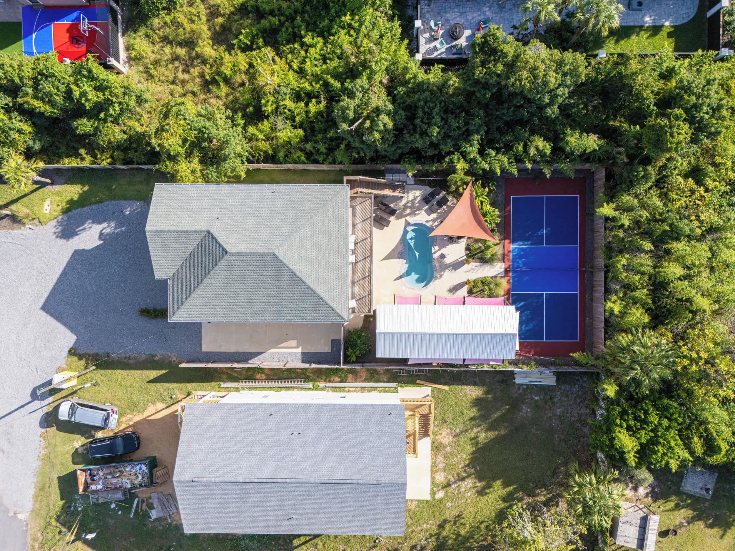 Vue aérienne d’un quartier résidentiel avec une maison, une piscine et un court de tennis.