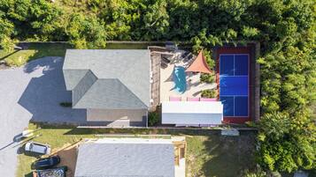 Vue aérienne d’un quartier résidentiel avec une maison, une piscine et un court de tennis.
