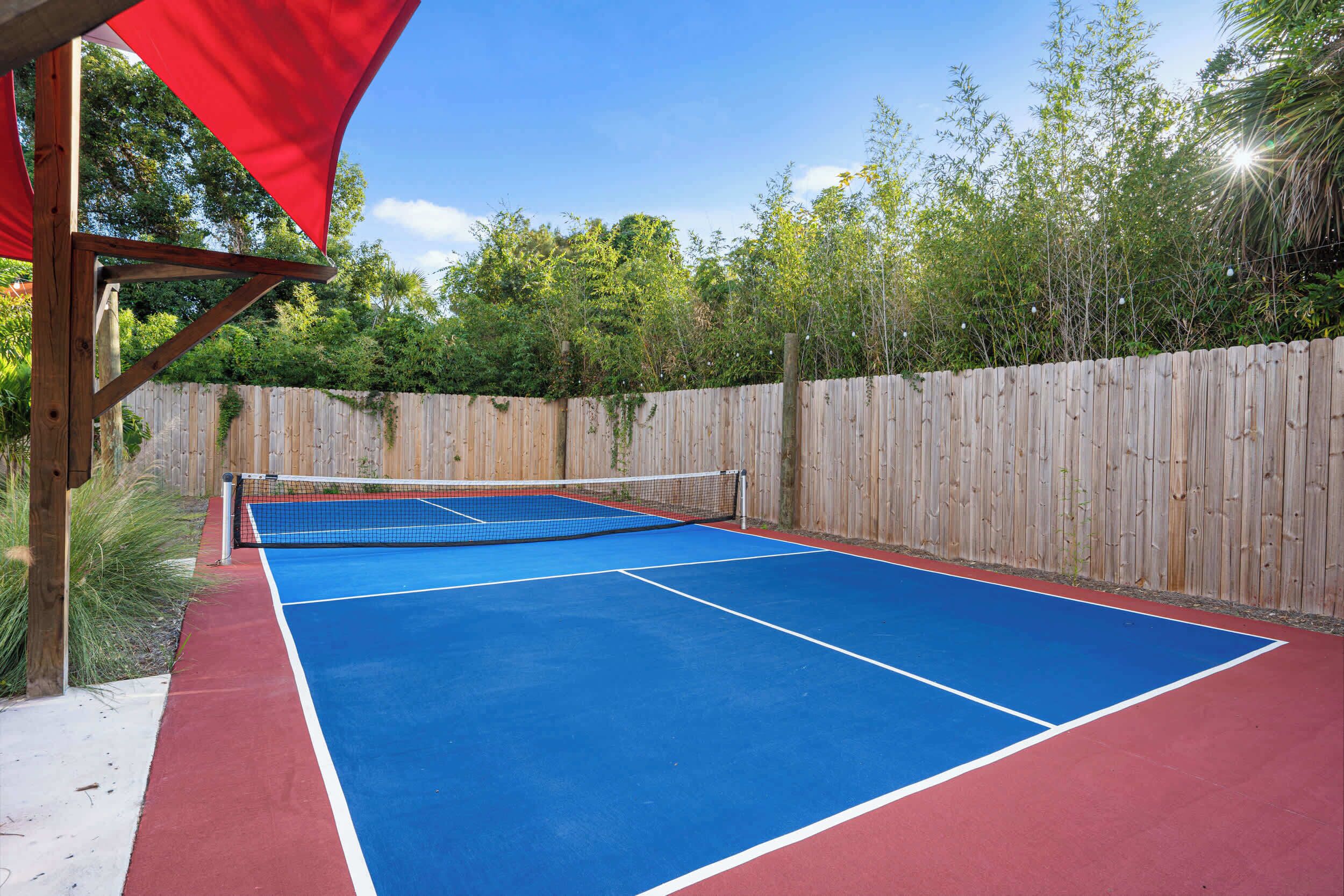 An outdoor tennis court with a wooden fence and a red canopy.