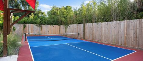 An outdoor tennis court with a wooden fence and a red canopy.