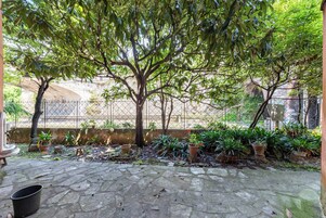 A courtyard with a large tree, potted plants, and a stone floor.