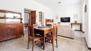 A dining area with a wooden table and chairs, a television, and a sofa in the living room. - Spacious 2-bedroom flat near the beach (Rapallo)