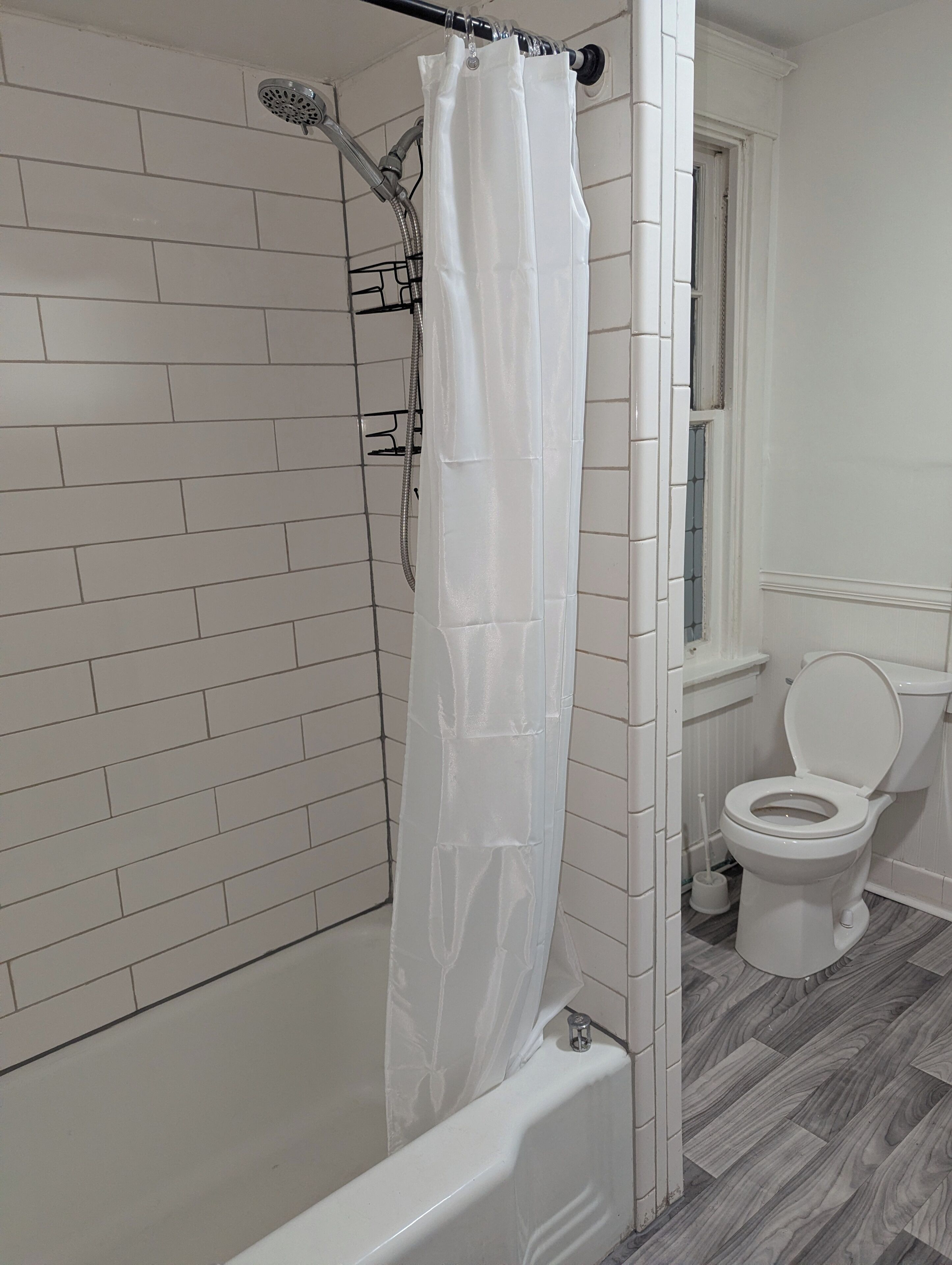 Een badkamer met een douche, toilet en een raam.