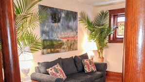 A living room with a blue sofa, two lamps, a painting, and potted plants.