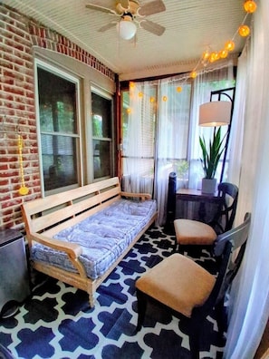A cozy room with a bed, a chair, a table, and a ceiling fan.