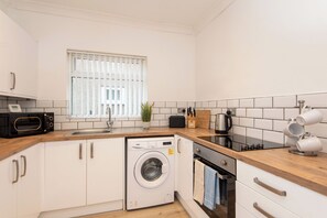 A compact kitchen with a washing machine, microwave, sink, and a window with blinds. - Toast Stays - Brankin Mill (Darlington)