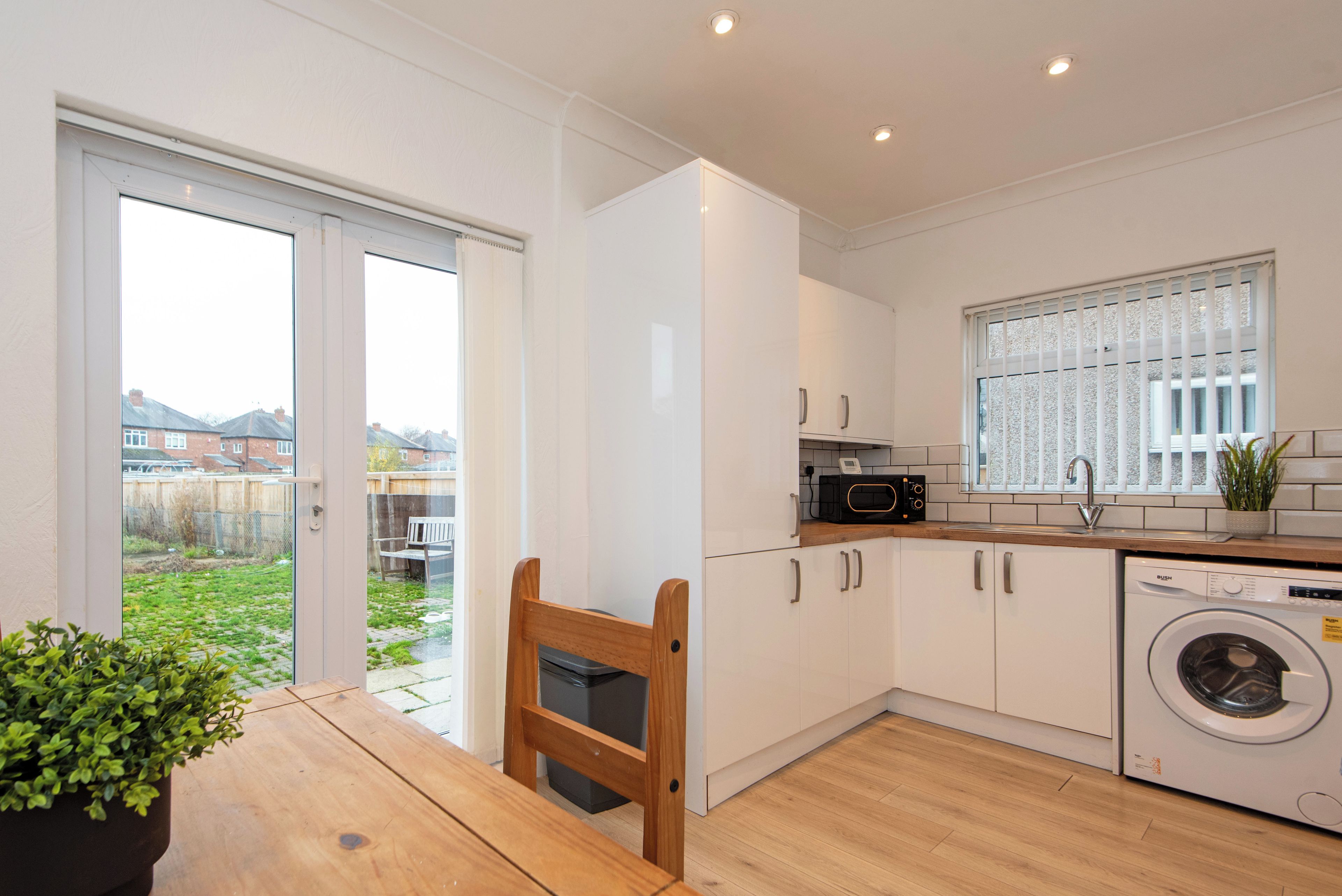 A modern kitchen with a built-in washing machine, a dining area with a wooden table, and a sliding glass door leading to a backyard.