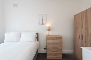 A bedroom with a bed, a wooden dresser, a nightstand, and a wall-mounted lamp. - Toast Stays - Brankin Mill (Darlington)