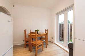 Un coin repas avec une table et des chaises en bois, une plante en pot et une vue à travers une porte vitrée.