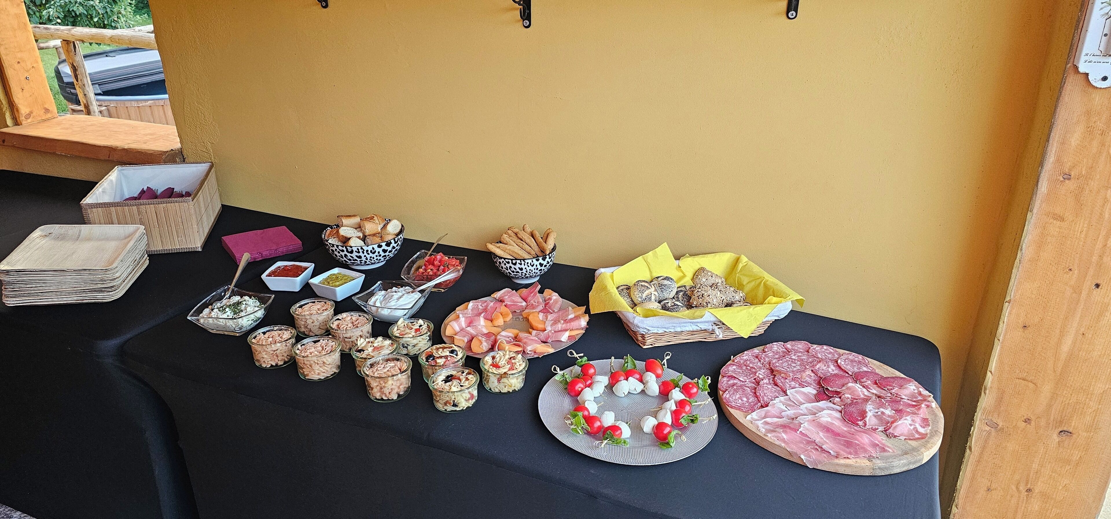 A table with various food items and condiments, including bread, cheese, and meats, arranged on a black tablecloth.