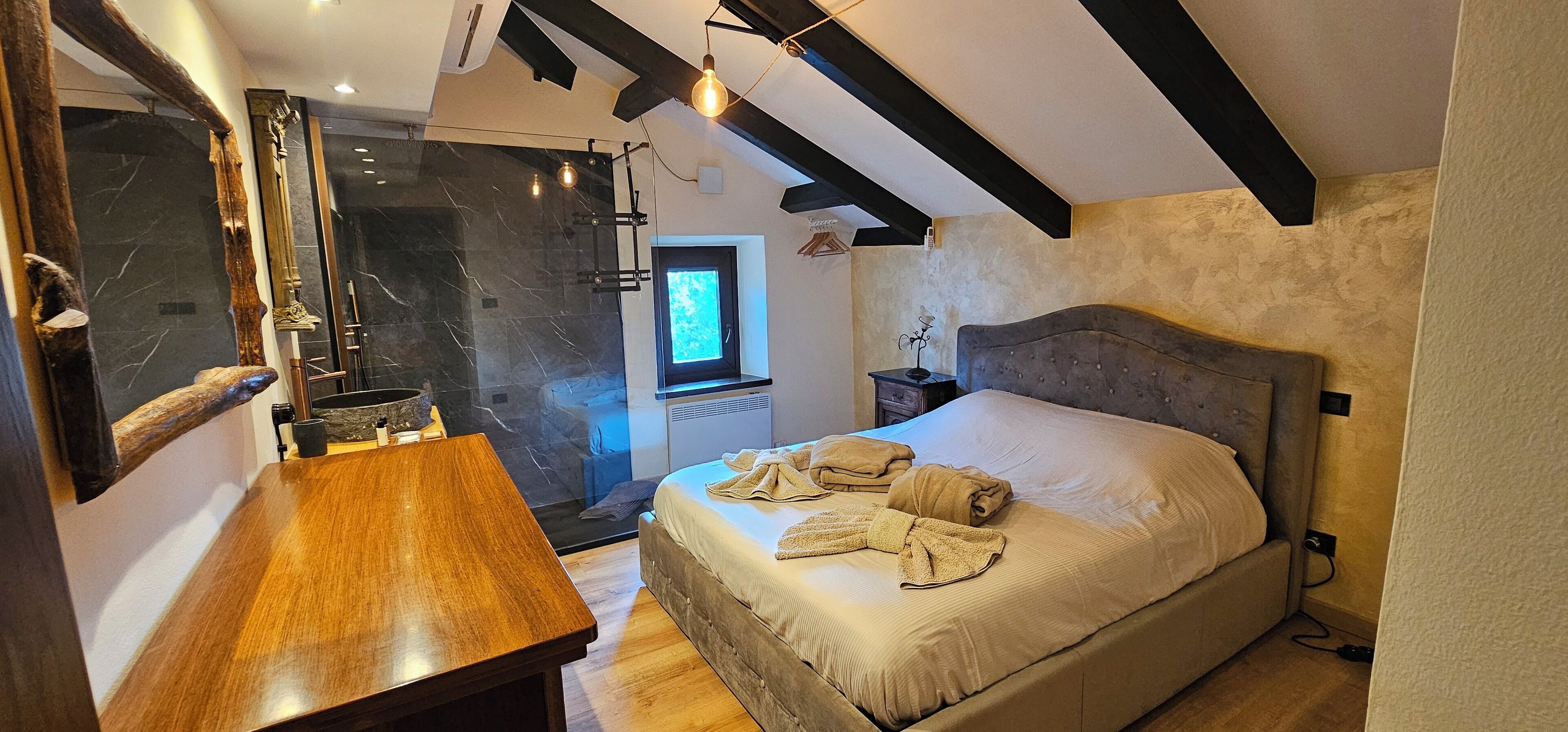 A bedroom with a large bed, a wooden desk, a mirror, and a window.