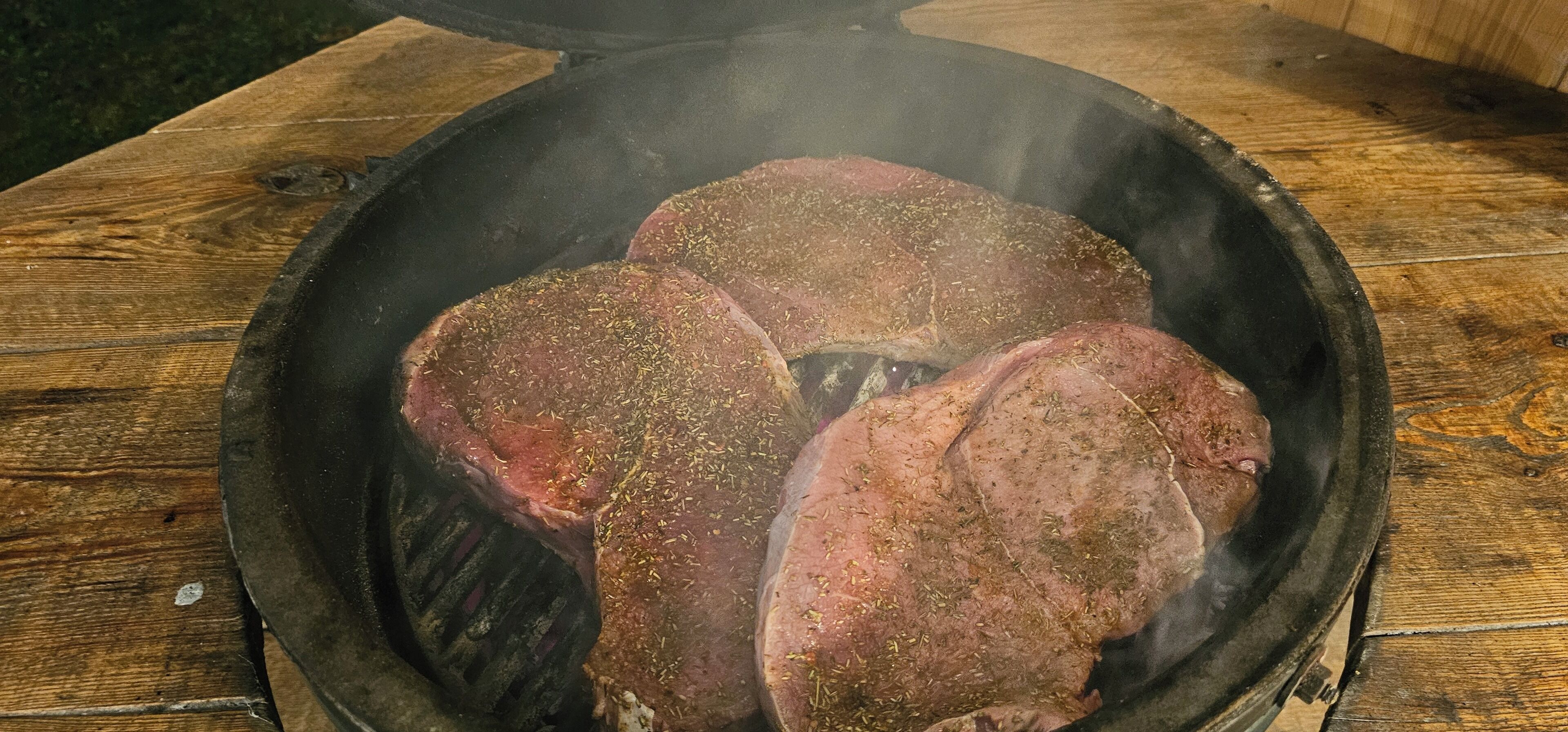 Steaks on a grill with a wooden table in the background.