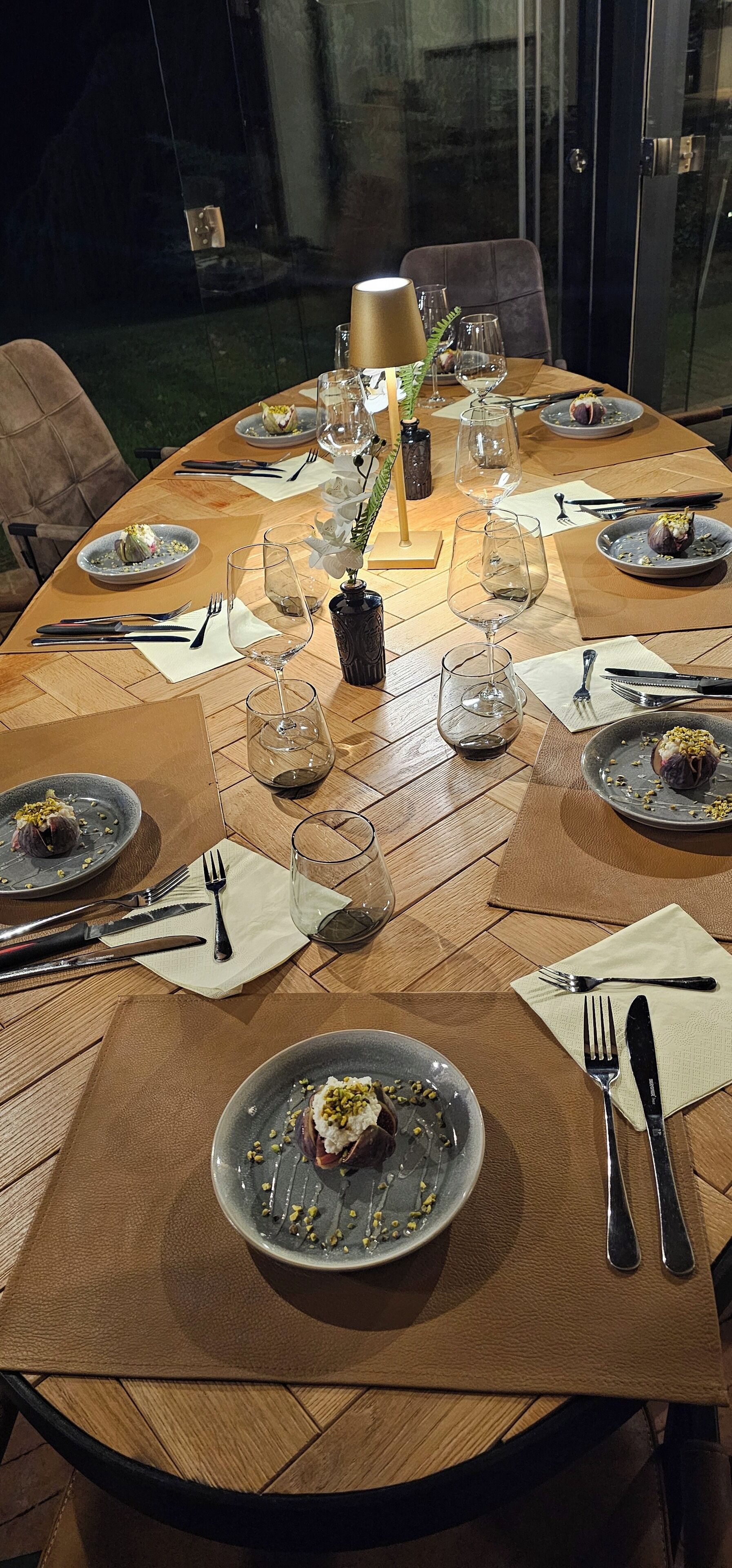 Een ronde eettafel gedekt voor een maaltijd, met borden, bestek en wijnglazen.