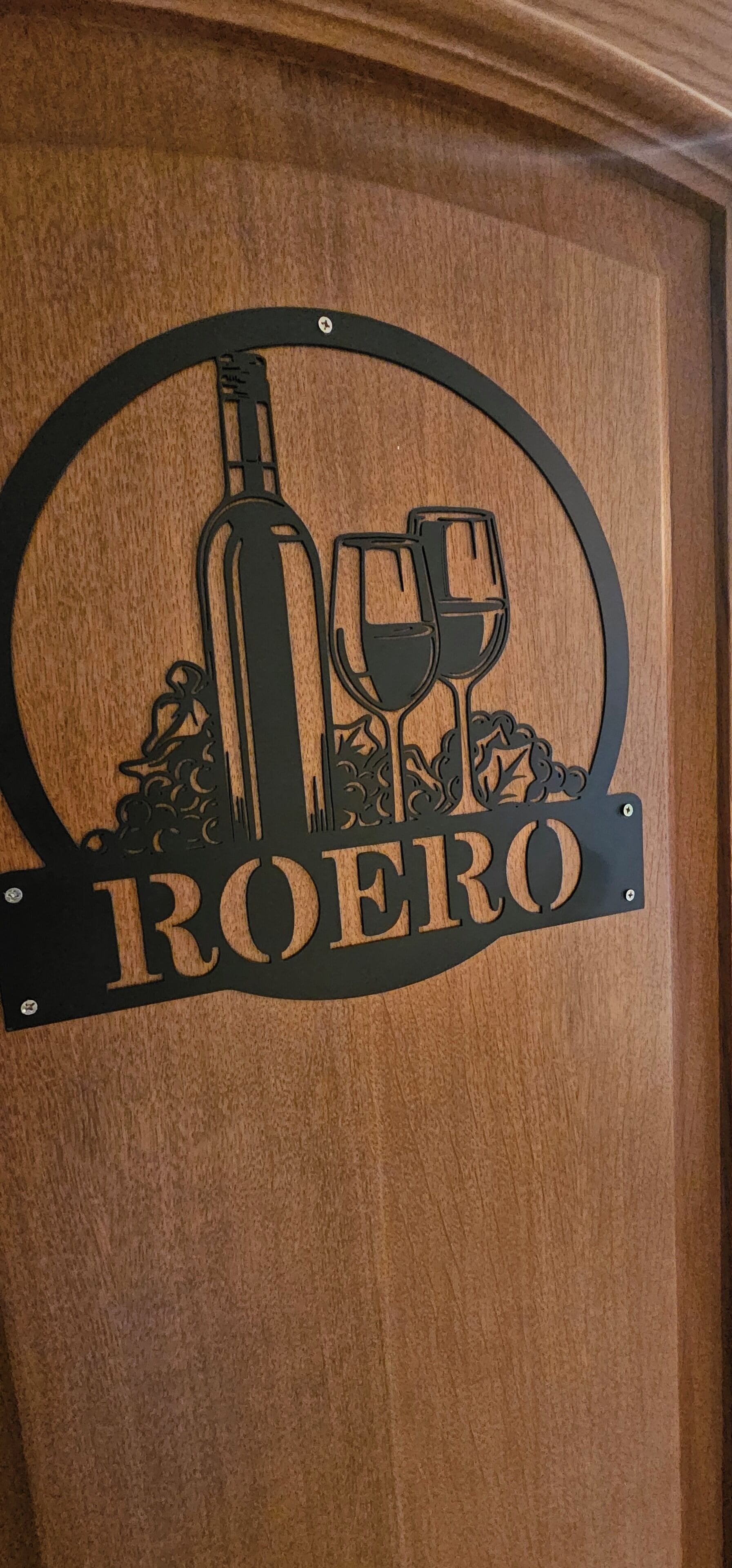 Un cartello di legno con una bottiglia di vino e calici, e il nome "ROERO".