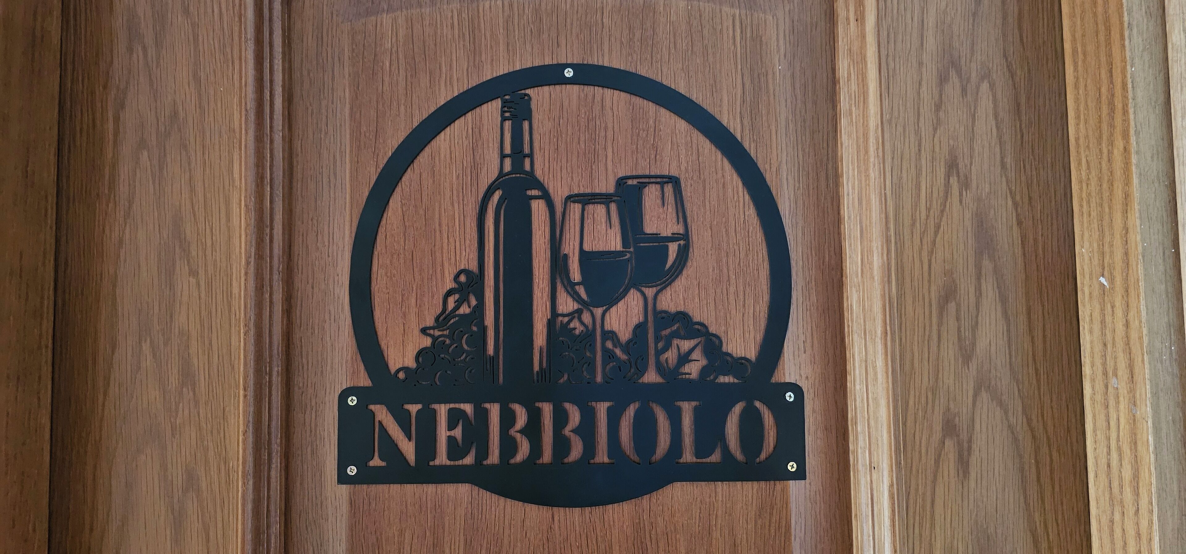 A wooden sign with a wine bottle and glasses, and the word "NEBBIOLO" on it.