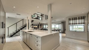 Una cocina amplia con una isla central, una escalera que lleva a un nivel superior y grandes ventanales con vistas.