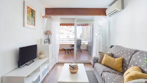 A living room with a TV, white furniture, a grey sofa with yellow cushions, a white coffee table, and a balcony with a view of buildings. - Apartment 'Los Olivos Bb' with Sea View, Wi-Fi and Air Conditioning (Faro de Cullera)