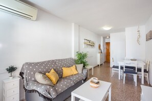 Un salon comprenant un canapé, une table à manger, des chaises, une petite table avec un panier, une plante en pot et un climatiseur fixé au mur.