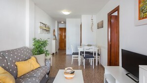 A living room with a sofa, a coffee table, a TV, and a dining area with chairs and a table. - Apartment 'Los Olivos Bb' with Sea View, Wi-Fi and Air Conditioning (Faro de Cullera)