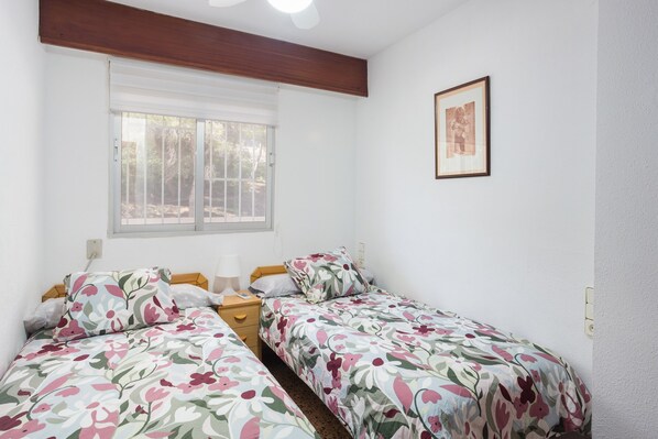 Un dormitorio con dos camas, una ventana, un cuadro enmarcado y una mesita de noche con una lámpara.