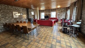 Ein geräumiges Zimmer mit Holzboden, Ziegelwand, Fliesenboden, einem großen Holztisch mit Stühlen, einem roten Sofa und einer Bar mit Sitzgelegenheiten.